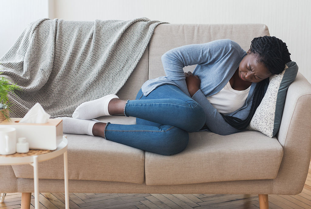 A Young African American Woman Lying on the Couch Clutching Her Stomach in Pain Fibroids vs Cysts