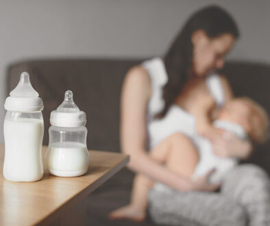 Closeup of Two Bottles Full of Milk With a Mother Breast Feeding Her Baby in the Background Increase Breast Milk Supply