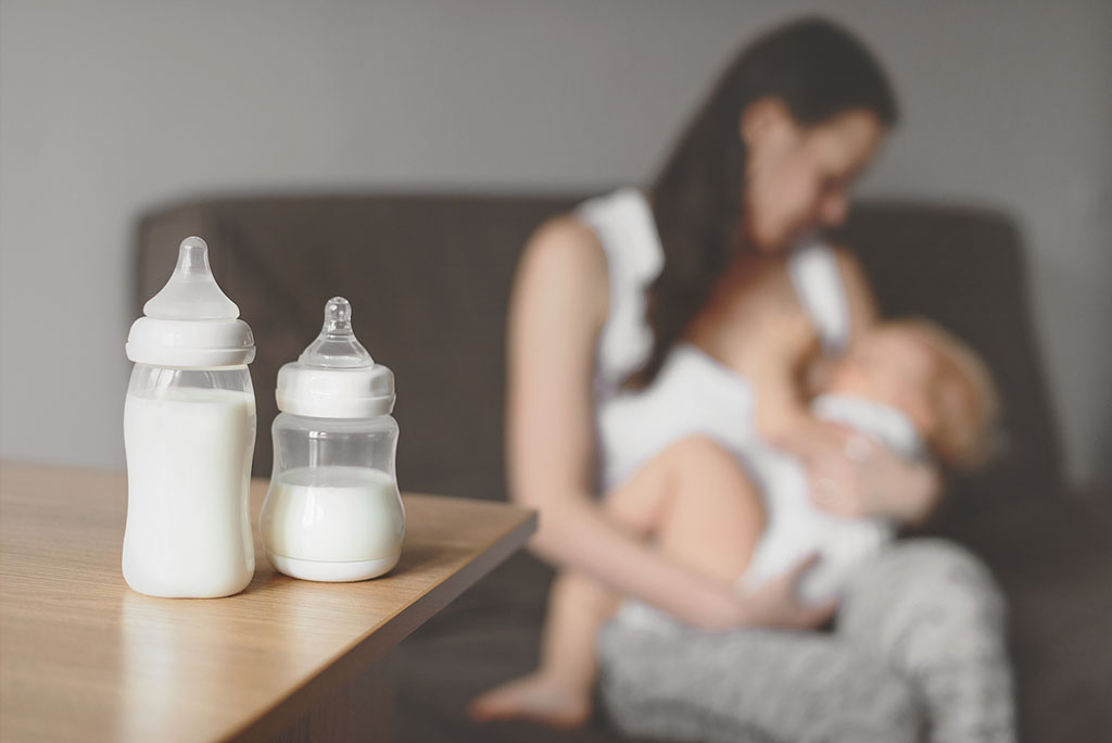 Closeup of Two Bottles Full of Milk With a Mother Breast Feeding Her Baby in the Background Increase Breast Milk Supply