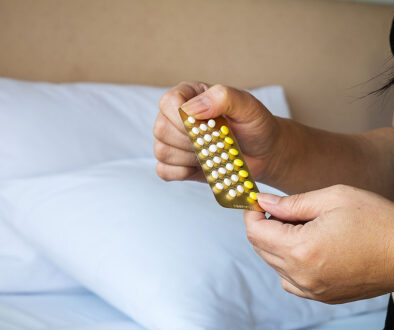 Closeup of a Woman Holding Birth Control Pills With a Bed in the Background Does Birth Control Affect Sex Drive