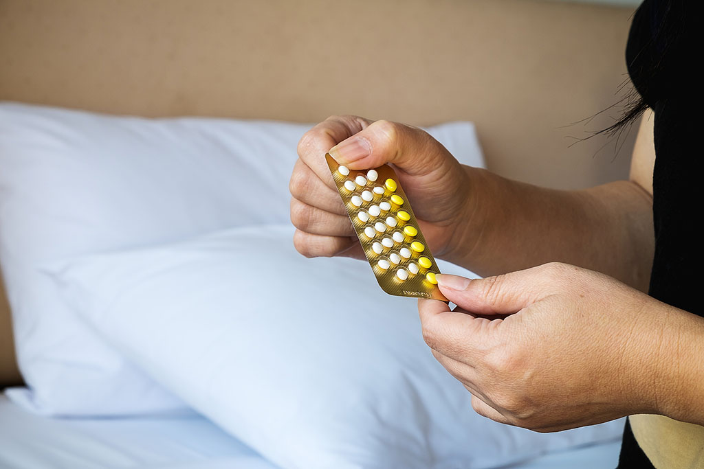 Closeup of a Woman Holding Birth Control Pills With a Bed in the Background Does Birth Control Affect Sex Drive