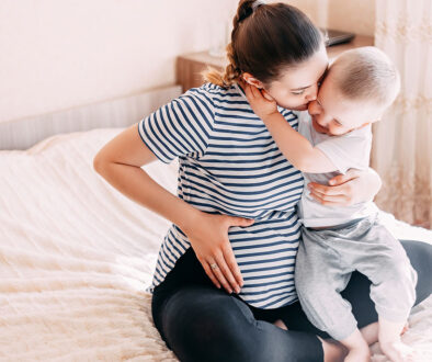 A Pregnant Mother Sitting on a Bed Hugging Her Other Child What Is Secondary Infertility